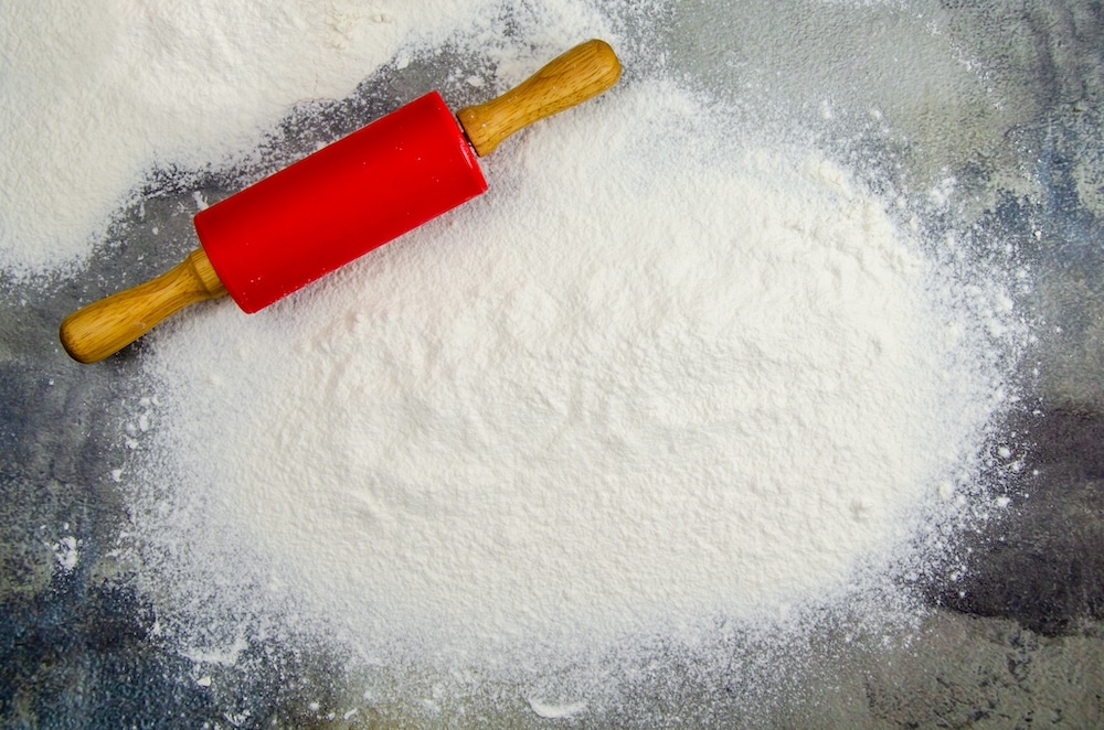 A pile of sifted flour and a rolling pin for rolling out the dough on a dark background of a concrete table top. Sprinkled flour on a cutting board. Space for text. Grainy surface, selective focus.